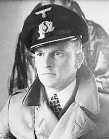 The head and shoulders of a young man, shown in semi-profile. He wears a greatcoat and his Iron Cross is visible at the front of his shirt collar. He wears a determined expression.