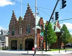 An ornate brick building with two large garages in front and two corresponding stepped point sections on the roof behind a traffic signal at the intersection of Delaware Avenue and Marshall Street, seen from the far corner.