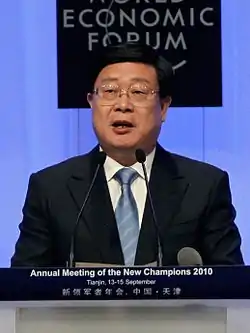 a man with a wavy haircut, wearing glasses, a white shirt, a suit and a blue tie