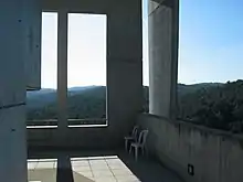 Two chairs on a concrete porch of a rectilinear building overlooking hills and green forest