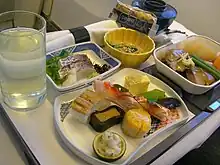 A picture with a glass of water on the left, a napkin on the top, with two bowls on the far right and three dishes in the center and right, all contained on a serving tray