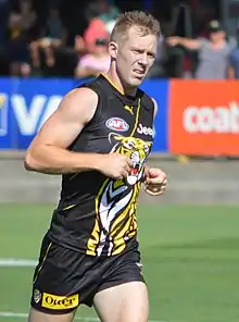 A light-brown-haired footballer in a sleeveless black tiger-emblazoned guernsey and shorts