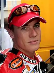 A man in his mid-20s wearing a red baseball cap and motorcycle overalls