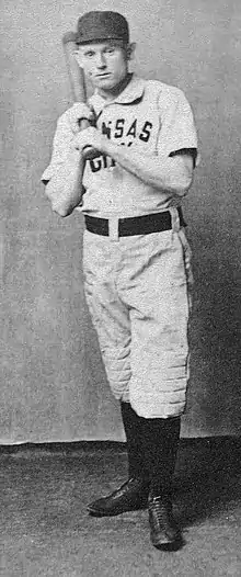 A baseball player is standing, holding a baseball bat.