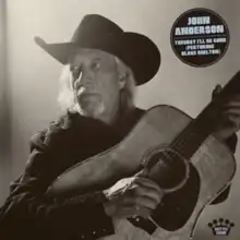 A black and white photograph of American singer John Anderson seated with his guitar resting in his arms; in the top right corner of the image is a circular-shaped black sticker that reads "John Anderson, Tuesday I'll Be Gone (Featuring Blake Shelton)" in an all-caps blue font.