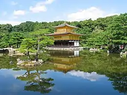 Moss covered ground in front of trees and a golden pavilion in the distance.