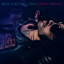 A picture of Kravitz wearing sunglasses reclining on a striped lounge in a dark room