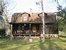 Front view of two-story log house in summer, with porch and dormer roof