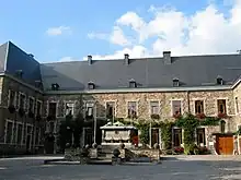 A courtyard is surrounded by a stone building, with ivy growing around wooden-framed windows.