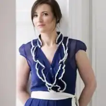 A photograph of Irish singer Margaret Healy wearing a blue dress and white belt. It is set against a white background.