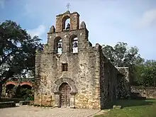 Small historic stone church building with three bells hanging above door