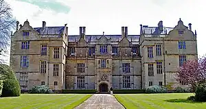 Facade of house built of yellow stone. Three floors with large, mullioned windows and Dutch gables to the roof.