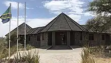 A view of the front entrance of the Olduvai Gorge Museum with a Tanzanian flag atop a flagpole in front of the building.