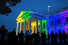 The White House lit with red, orange, yellow, green, blue, and violet lights.