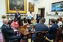 Photo of Biden and staffers, seated, looking at a television