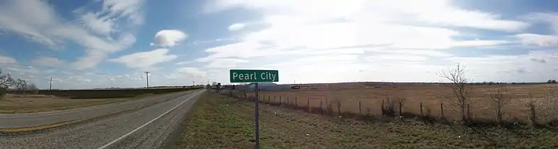 A rural road with the Pearl City sign in the foreground.  A few small buildings are barely visible in the distance.