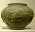 A green-grey bowl with a small bottom, a very wide center, and a top opening wider than the base but not as wide as the center. A pattern of out-dented large leaves covers the body of the bowl.