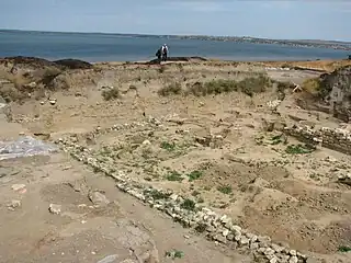 The remains of the wall of a small structure are seen in the foreground, the Sea of Azov is visible in the background.