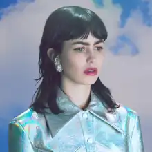 A dark haired white woman wearing a holographic blue coat