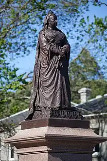 A bronze statue of Queen Victoria atop a granite pedestal, holding a fan.