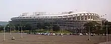  A large circular stadium with a curving overhang behind a mostly empty parking lot.