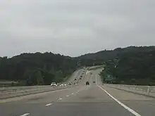 Downhill view of a four-lane divided freeway; the opposing lanes of traffic are separated by concrete barriers.