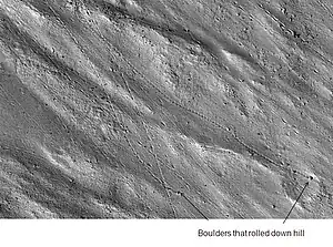 Enlargement of cliff in the Kasei Valles system in previous image showing boulders and their tracks, as seen by HiRISE. The boulders are around 2 m across.