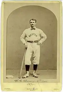 A mustachioed man in a dark jacket with a broad collar, white shirt, and dark tie.