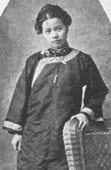 A young Chinese woman, standing, wearing a dark tunic