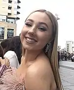 Woman with blonde hair smiling for the camera, wearing a pink fluffy dress