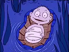 A smiling cartoon baby lying in a basket filled with bottles, floating on water from which rushes grow.