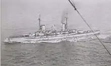 A light gray battleship steams in choppy seas.