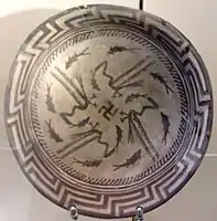 Samarra plate, with a design consists of a rim, a circle of eight fish, and four fish swimming towards the center being caught by four birds, at the center being a swastika symbol; circa 4000 BCE; painted ceramic; diameter: 27.7 cm; Vorderasiatisches Museum (Berlin)