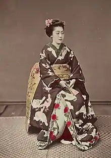 Photographic portrait of a young woman wearing a layered long-sleeved kimono and a trailing darari obi.