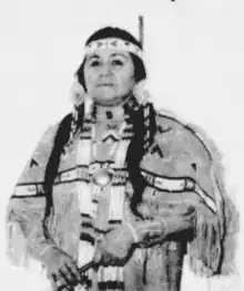 Image of a Native woman wearing beaded and fringed buckskins and holding a pipe in her lowered hands