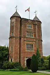 a high tower of red brick with two pyramid roofs and a flag flying