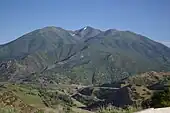 a river is in the center of the picture, with a canyon wall and mountains visible on the right side. To the left of the river is a black streak, remains of a rail line. To the right of the river is an abandoned road, with a new road and rail line in cuts along the canyon wall.