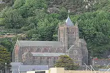 A large church standing before a hillside, with a clerestory and, to the left a tower with a pyramidal roof.