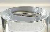 A metal paper clip floats on water. Several can usually be carefully added without overflow of water.