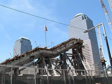 A few flights of concrete stairs, their underlying support stripped and replaced with steel beams, seen behind a chainlink fence.