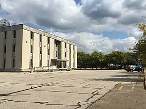 A three-story building with a brick facade sits to the left in the picture, with an empty parking lot in the foreground. To the far right, a small black van with "97.5 WONE" is parked in the lot.