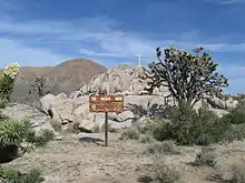 Rocky outcropping with a cross on top, tree and sign in foreground