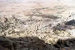 A viewing point overlooking a monotone town in a desert valley with sparse vegetation nearby