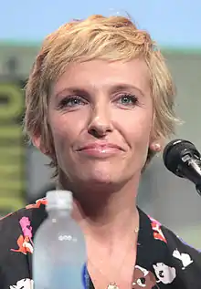 A photograph of Toni Collete. She has strawberry-blonde, over-shoulder length hair. She has a black jacket over a white dress, which has black polka dots.