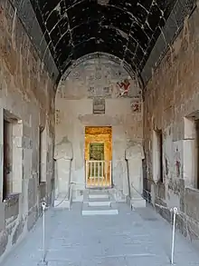 Hall with a vaulted ceiling, all covered in painted artwork, and a pair of stone statues