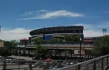 View from the Mets-Willets Point station's platform, with the former Shea Stadium in the background. A black fence, which surrounds the platform, is visible on the bottom right corner.