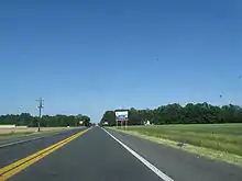 A two-lane road passing through farm fields. A blue and white sign on the right indicates an ongoing construction project on US 113.