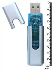 A USB thumb drive and its cap, next to a 100 millimeter ruler for scale