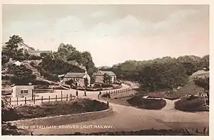 Two houses and a small station building at the curved railway behind a fence