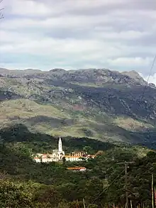 Building with tall spire nestled at the foot of a mountain range in the background